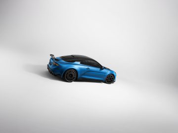 Op een gladde, lichtgrijze ondergrond staat een Alpine A110 R-sportwagen met zwart dak en spoiler geparkeerd. De blauwe auto wordt bekeken vanuit een hoge driekwarthoek aan de achterkant.