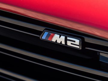 Close-up van het embleem op een BMW M2, waarbij het strakke ‘M2’-logo tegen de zwarte grille wordt benadrukt.