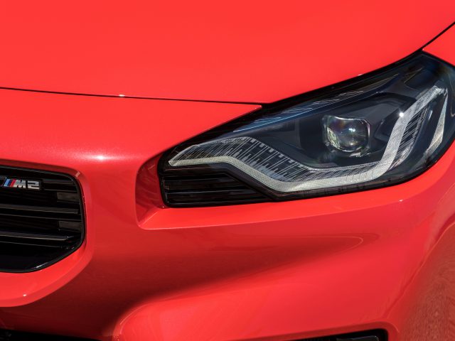 Close-up van de koplamp linksvoor en een deel van de grille van een rode BMW M2.