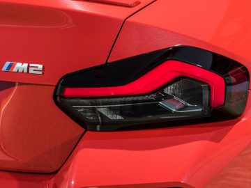 Close-up van het achterlicht en de badge van een rode BMW M2, met het opvallende achterlichtontwerp en het iconische M2-embleem.