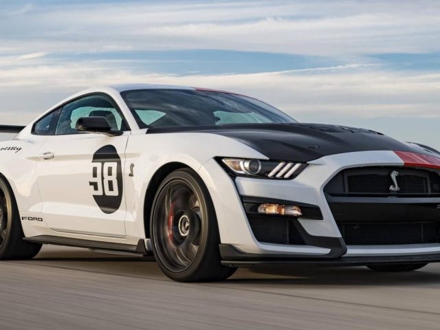 Een witte, zwarte en rode Ford Mustang-sportwagen met het nummer 98 op de deur wordt met hoge snelheid over een weg gereden.
