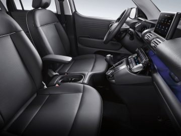 Binnenaanzicht van een moderne Hyundai Casper met zwartleren stoelen, een middenconsole met armleuningen en bekerhouders, en een digitaal dashboard met bedieningselementen en displays.