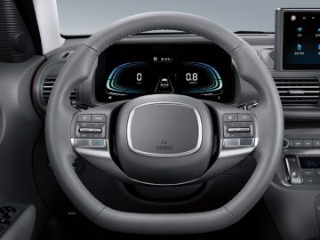 Close-up van het stuur en het dashboard van een Hyundai Casper, met verschillende bedieningsknoppen en een digitaal display achter het stuur. Het display toont voertuiginformatie en navigatiedetails met indrukwekkende helderheid.