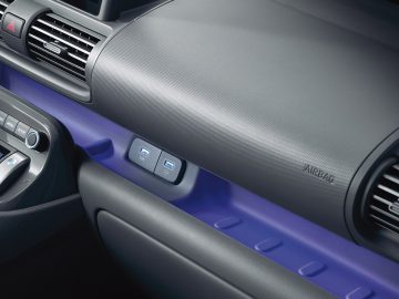 Close-up van een Hyundai Casper-dashboard met ventilatieopeningen, een bedieningspaneel met knoppen en een compartiment met twee USB-poorten. Het woord "AIRBAG" is zichtbaar op het dashboard.