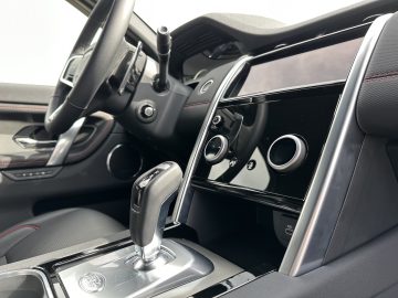 Binnenaanzicht van de Land Rover Discovery Sport P300e met het stuur, de versnellingspook en een strak dashboard met touchscreeninterface en bedieningsknoppen.