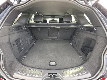 Een blik op de ruime bagageruimte van een Land Rover Discovery Sport P300e met neergeklapte achterbank en een beschermende bagageafdekking. Het interieur is strak met donkere bekleding en metalen afwerking.