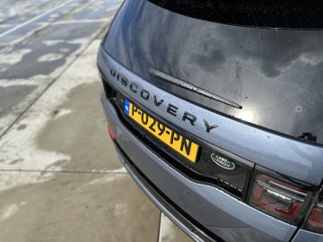 Close-up van de achterkant van een Land Rover Discovery Sport P300e met een gele kentekenplaat met de tekst "P029 PN", geparkeerd op een nat betonnen oppervlak.