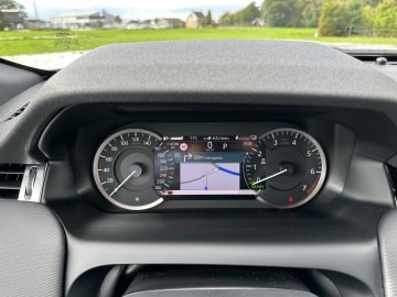 Close-up van een Land Rover Discovery Sport P300e-dashboard, met snelheidsmeter, kilometerteller, brandstofmeter en een centraal scherm met een navigatiekaart en waarschuwingsborden.