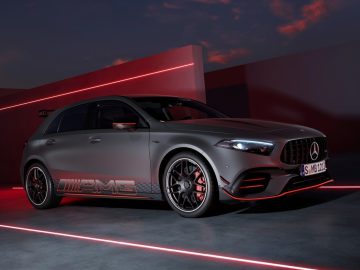 Een slanke, donkergekleurde Mercedes-Benz A-Klasse hatchback staat geparkeerd in een futuristische omgeving met rode en roze sfeerverlichting, met het AMG-logo en stijlvolle lichtmetalen velgen.