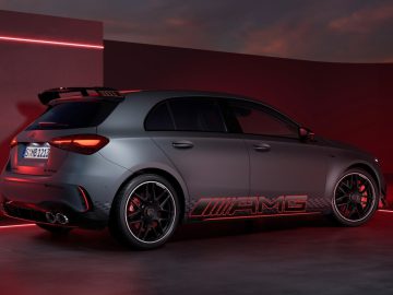 Een matgrijze compacte sportwagen van Mercedes-Benz A-Klasse met een zwarte dakspoiler en rode accenten, geparkeerd in een slecht verlichte kamer, waar het AMG-merk en de kenmerken ervan goed tot uiting komen.