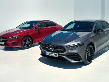 Twee Mercedes-Benz A-Klasse-auto's staan geparkeerd op een witte ondergrond. De ene is rood en de andere is grijs, beide vanuit een kleine hoek gezien vanaf de voorkant.