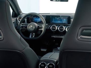 Binnenaanzicht van een Mercedes-Benz A-Klasse met het stuur met het iconische logo, een digitaal dashboard, dubbele klimaatregelingsknoppen en zachte zwartleren stoelen.