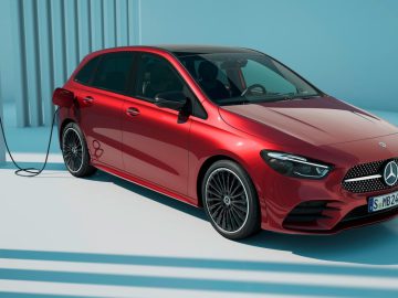 Een strakke rode Mercedes-Benz A-Klasse elektrische auto is aangesloten op een laadstation tegen een lichtblauwe achtergrond met schaduwen.