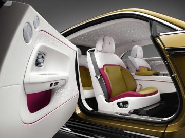 Het interieur van een Rolls-Royce Spectre met open deuren is voorzien van witleren stoelen met bruine en roze accenten, verlichte panelen en moderne bedieningselementen.