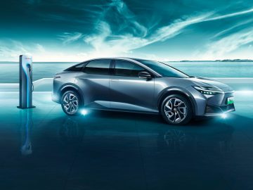 Een elektrische auto van Toyota bZ3 aangesloten op een laadstation, met een achtergrond van kalme zee en lucht onder witte wolken.