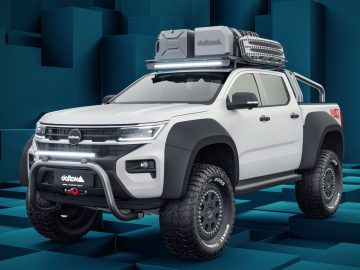Een witte Volkswagen Amarok Delta4x4 offroad-truck uitgerust met een imperiaal, reservewiel en bullbar aan de voorkant staat geparkeerd op een geometrische blauwe achtergrond.