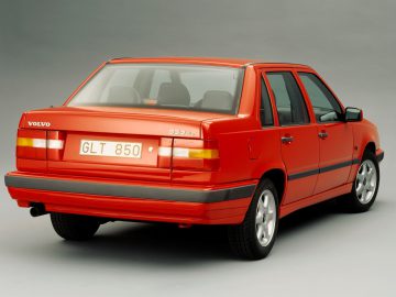 Een rode Volvo 850 GLT sedan met een kentekenplaat met de tekst "GLT 850", vanaf de achterkant gezien tegen een effen achtergrond.