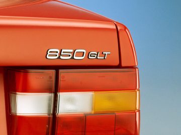 Close-up van het achterlicht en het kenteken van een oranje Volvo 850 GLT-auto. Op de badge staat trots '850 GLT', terwijl het achterlicht levendige rode, oranje en witte delen heeft.