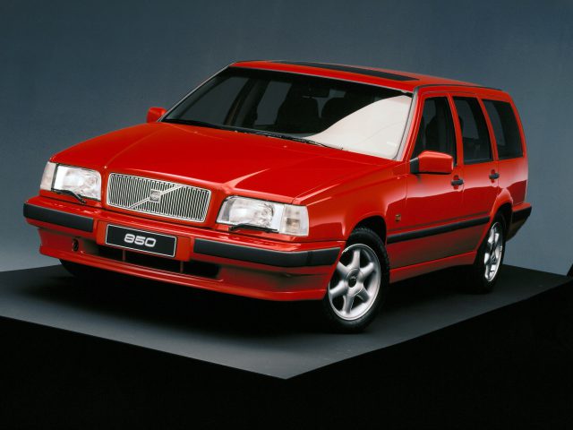 Op een perron tegen een donkere achtergrond staat een Volvo 850 stationwagen, geschilderd in opvallend rood.