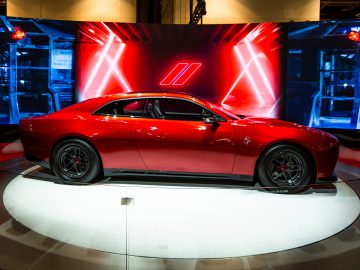 Een glanzend rode Dodge Charger Daytona SRT wordt tentoongesteld op een roterend platform, tegen een achtergrond van neonrode en blauwe lichten.