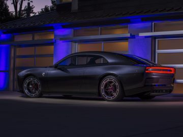 Een strakke zwarte Dodge Charger Daytona SRT staat geparkeerd voor een garage met blauwe accentverlichting, waardoor in de schemering het zij- en achteraanzicht zichtbaar is.