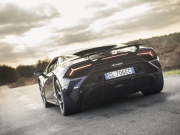 Achteraanzicht van een zwarte Lamborghini-sportwagen met kenteken "GL-706EC", geparkeerd op een landelijke weg onder een bewolkte hemel.