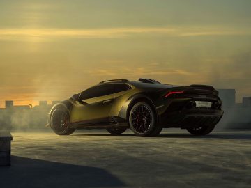 Een metallic groene sportwagen staat geparkeerd op een dak met een zonsondergang op de achtergrond en mist eromheen. Op het kenteken staat "Lamborghini Huracán Sterrato", wat het model van de auto aangeeft.