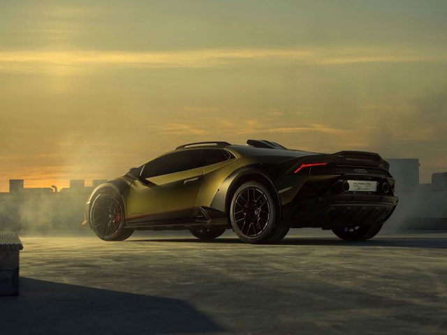 Een metallic groene sportwagen staat geparkeerd op een dak met een zonsondergang op de achtergrond en mist eromheen. Op het kenteken staat "Lamborghini Huracán Sterrato", wat het model van de auto aangeeft.