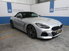 Een zilverkleurige BMW-cabriolet staat binnen geparkeerd met op de achtergrond een blauw-wit spandoek met de tekst 'Domeinen Roerende Zaken Ministerie van Financiën', wat een scène oproept die Sywert wellicht op prijs stelt.