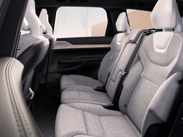 Een zicht op het interieur van de achterbank van een Volvo EX90, met lichtgrijze stoffen bekleding, drie hoofdsteunen en veiligheidsgordels.