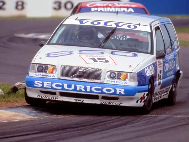 Een Volvo 850-raceauto met het nummer 15 op de grille, gesponsord door Securicor, rijdt tijdens een race-evenement de bocht om. Een andere Volvo 850 volgt op de voet.