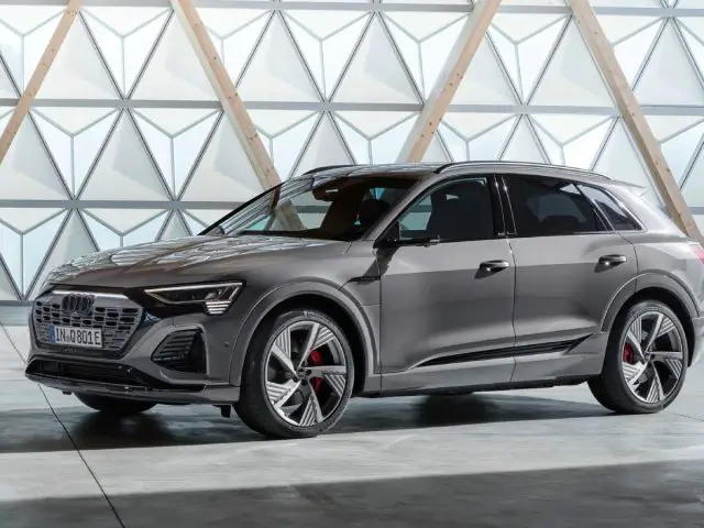 Een grijze vierdeurs Audi Q8 e-tron SUV staat geparkeerd in een moderne showroom met geometrische muurpatronen op de achtergrond.