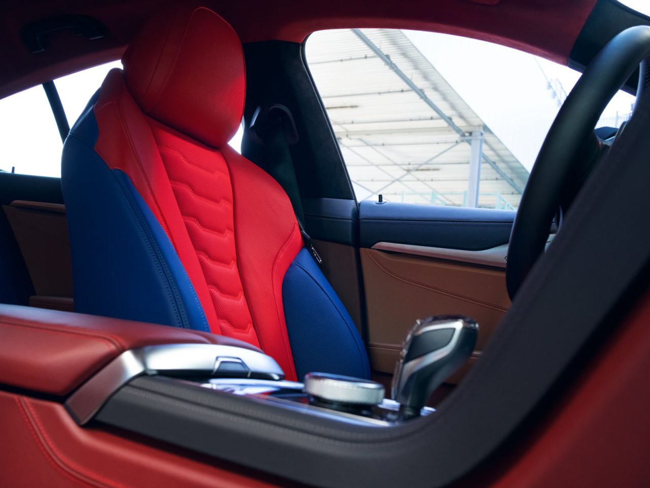 Binnenaanzicht van THE 8 X JEFF KOONS-auto met de bestuurdersstoel met rode en blauwe bekleding, middenconsole en een deel van het stuur.