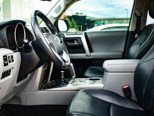 Interieur van een SUV met een leren stuur, dashboardbediening, versnellingspook en twee leren stoelen. De autodeur staat open, waardoor u door de ramen zicht naar buiten heeft. Deze modellen brengen een mix van luxe en functionaliteit in uw rijervaring.