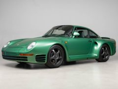 Groene Porsche-sportwagen met een strak ontwerp, opvallende koplampen en zwarte velgen, geparkeerd op een lichtgekleurd oppervlak voor een effen achtergrond.
