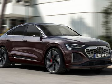 Een donkerrode Audi Q8 e-tron Sportback rijdt door een straat met vage gebouwen op de achtergrond.