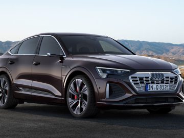 Een donkerrode Audi e-tron GT staat geparkeerd op een verhard oppervlak met een bergachtig landschap op de achtergrond, wat de elegantie en innovatie laat zien die de Audi-familie deelt, inclusief de Audi Q8 e-tron.