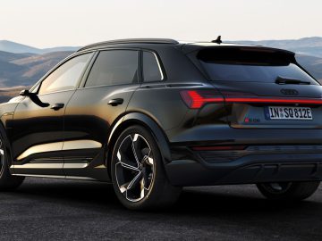 Een zwarte Audi Q8 e-tron SUV staat geparkeerd op een weg met een bergachtig landschap op de achtergrond onder een heldere hemel.