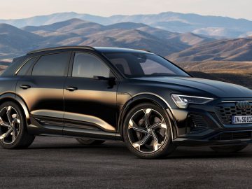 Een zwarte Audi Q8 e-tron SUV staat geparkeerd op een betonnen ondergrond met een achtergrond van glooiende heuvels onder een heldere hemel.