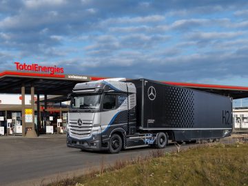 Bij een TotalEnergies-tankstation staat een grote waterstof-aangedreven Mercedes-Benz vrachtwagen geparkeerd onder een gedeeltelijk bewolkte hemel.