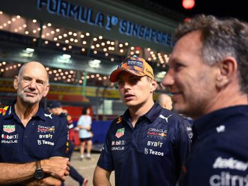 Drie mannen in teamkleding staan te praten voor een verlichte achtergrond van de Formule 1 in Singapore, waarbij de invloed van Adrian Newey duidelijk zichtbaar is in de technische discussies.