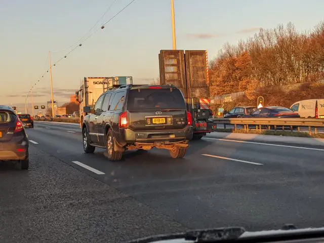 Een zwarte Infiniti SUV die op een snelweg rijdt, omringd door andere voertuigen, met een vrachtwagen er recht voor en bomen op de achtergrond verlicht door de ondergaande zon.