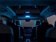 Binnenaanzicht van een auto met een panoramisch schuifdak en blauwe sfeerverlichting, met stoelen in twee rijen. Het dashboard, verlicht door subtiel ultraviolet licht, is in de verte zichtbaar.