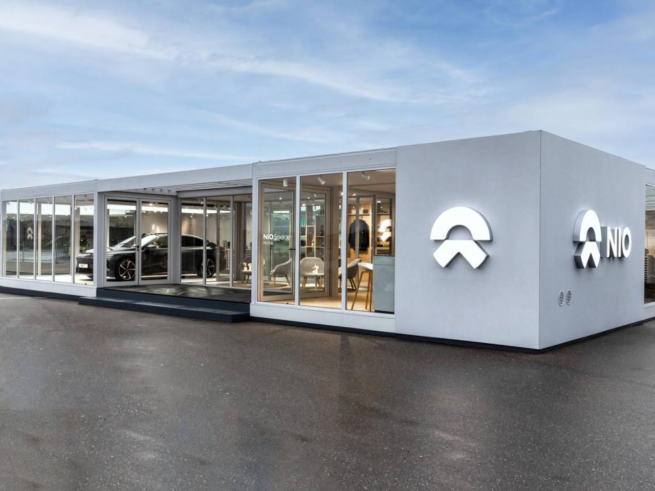 In een moderne showroom met glazen wanden worden de strakke elektrische voertuigen van Nio tentoongesteld. Het gebouw toont trots het logo en de naam van het bedrijf en nodigt voorbijgangers uit om de toekomst van autorijden te verkennen.