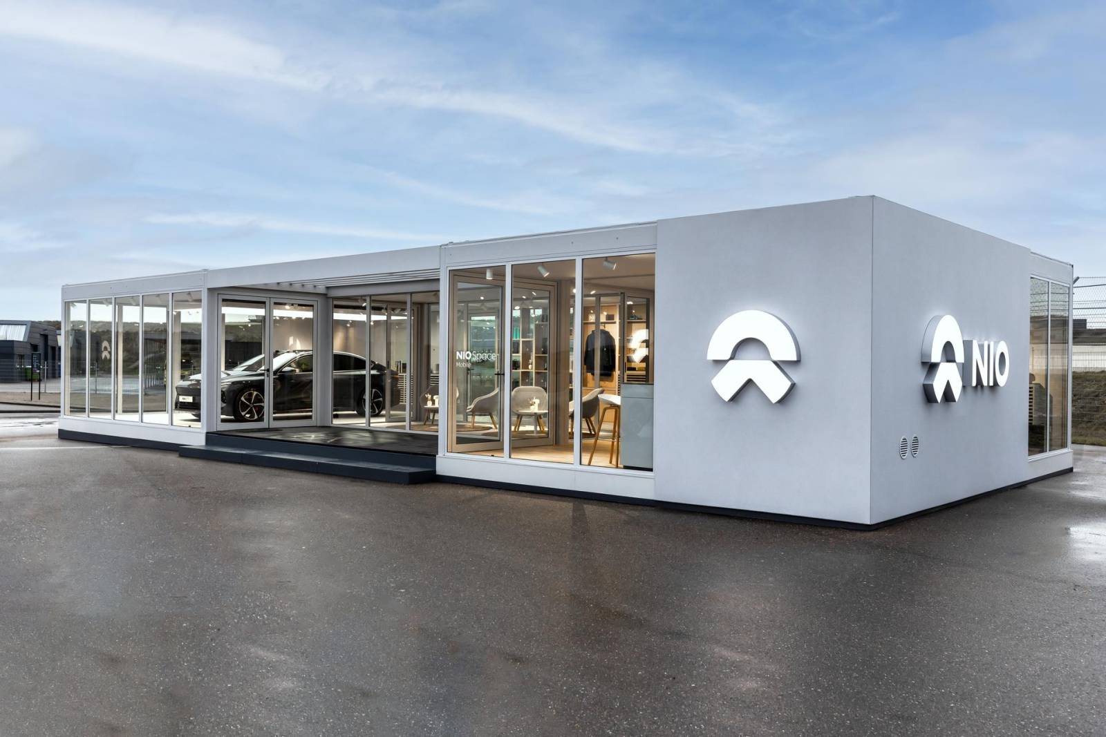 In een moderne showroom met glazen wanden worden de strakke elektrische voertuigen van Nio tentoongesteld. Het gebouw toont trots het logo en de naam van het bedrijf en nodigt voorbijgangers uit om de toekomst van autorijden te verkennen.