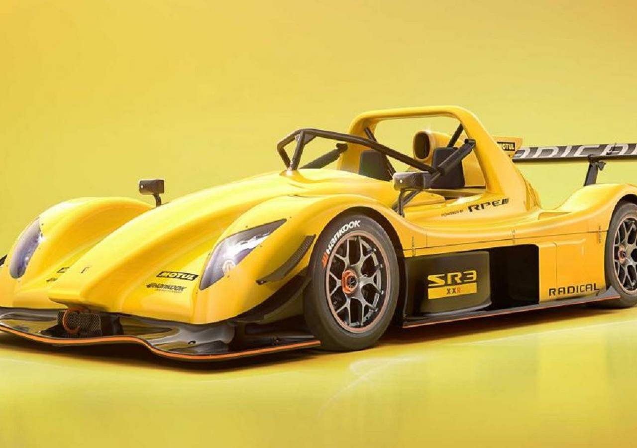 Een felgele Radical SR3 XXR-raceauto staat geparkeerd tegen een gele achtergrond met kleurverloop, waardoor de aerodynamische carrosserie, zijvleugel en gedetailleerde wielen goed tot hun recht komen.