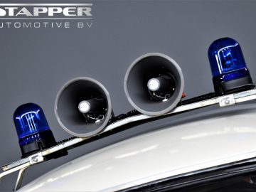 Close-up van blauwe noodlichten en sirenes op het dak van een voertuig met op de achtergrond het logo "STAPPER AUTOMOTIVE BV", dat doet denken aan een klassieke Trabant P601.