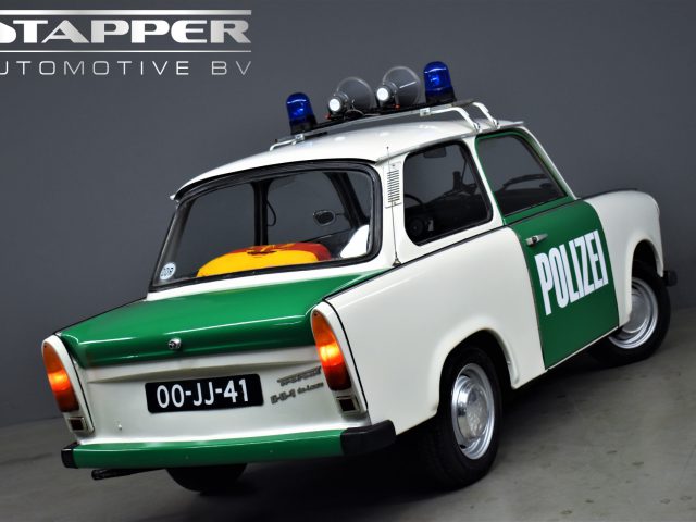 Een kleine vintage politieauto, een Trabant P601 met groene en witte verf, met het opschrift "Polizei", wordt tentoongesteld in een showroom. De auto heeft een kenteken met de tekst "00-JJ-41" en noodverlichting op het dak.
