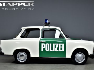 Zijaanzicht van een klassieke groen-witte Trabant P601-politieauto met "Polizei" op de deur geschreven, weergegeven voor een grijze achtergrond met het "Stappert Automotive BV"-logo in de linkerbovenhoek.