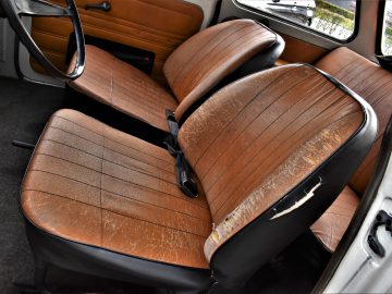 Het interieur van een oude Trabant P601 met versleten bruinleren stoelen en een stuur. De rugleuningen en zittingen vertonen aanzienlijke slijtage, en één zitting heeft een zichtbare scheur.